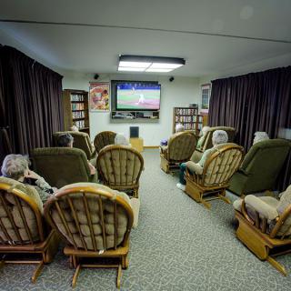 A cozy living room with several chairs arranged around a TV screen, where people are gathered watching a show.