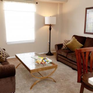 A cozy living room with a brown sofa, wooden coffee table, and a floor lamp by the window.