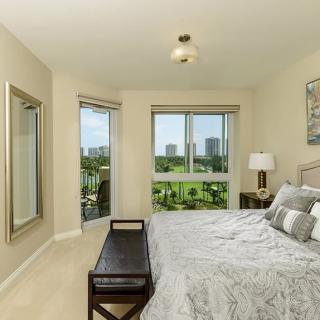 A modern bedroom featuring a large bed, neutral decor, and a view of the city through large windows.