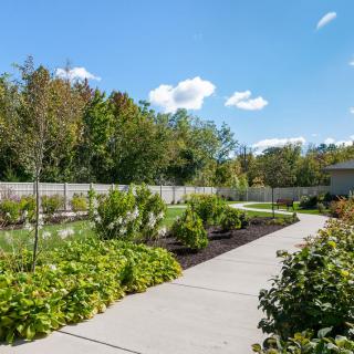 A beautifully landscaped garden with a paved pathway leading through vibrant plants and greenery under a clear blue sky.