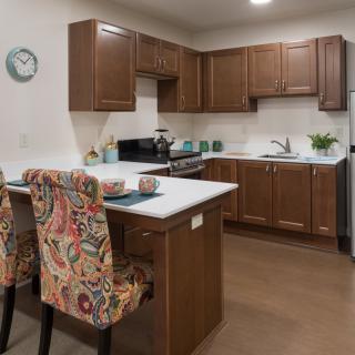 A cozy kitchen with wooden cabinets, a central island with floral upholstered chairs, and modern appliances.
