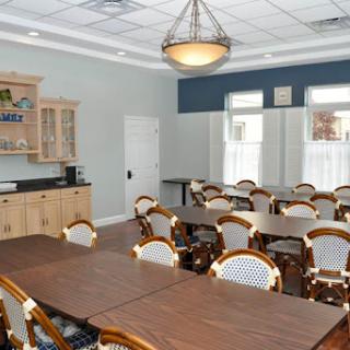 A spacious meeting room equipped with tables and chairs, featuring a kitchenette area.