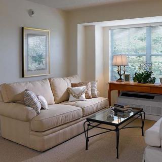 A cozy living room with a beige sofa, glass coffee table, and a bright window.