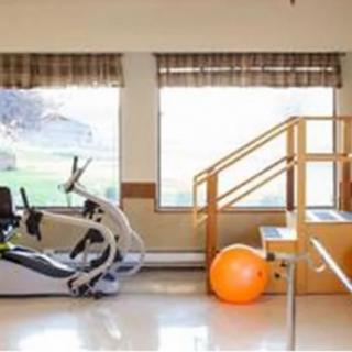 A physical therapy room with an exercise bike, an orange exercise ball, and a set of stairs with a handrail.