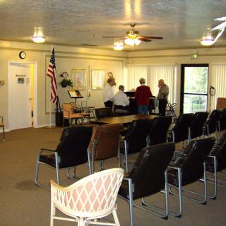 A community center meeting room with chairs arranged and a group of people around a piano.