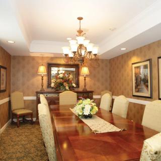 A formal dining room with elegant decor, featuring a large wooden table and upholstered chairs under a chandelier.