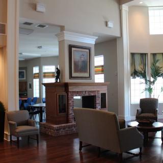 A cozy living room with a central fireplace, surrounded by comfortable seating and ample natural light from large windows.