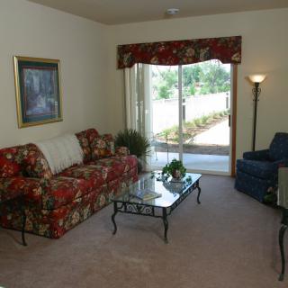 A cozy living room with a floral sofa set, glass coffee table, and sliding glass door leading to the outside.
