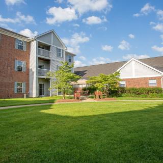 An exterior view of an apartment building with a well-maintained lawn under a partly cloudy sky.