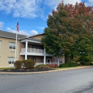 A two-story building with a flagpole in front, surrounded by trees and under a partly cloudy sky.