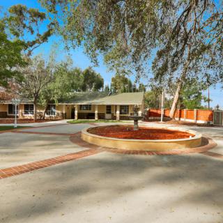 A school building surrounded by trees with a circular driveway in front.