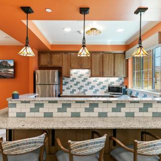 A modern kitchen with orange walls, featuring a bar counter and pendant lights.