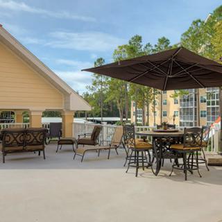 A spacious outdoor patio with tables, chairs, and an umbrella, surrounded by trees and adjacent to a building.