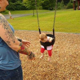 A playful moment at the park where a child enjoys swinging while a parent watches closely.