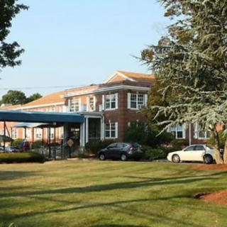 A brick building with a well-maintained lawn and trees, featuring two cars parked outside.