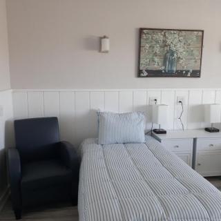 A neatly arranged bedroom with a single bed, chair, nightstand, lamps, and wall artwork.