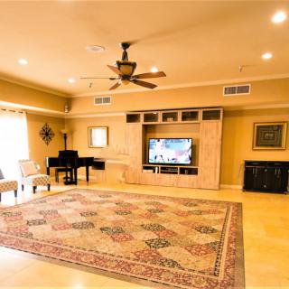 A spacious living room featuring a grand piano, television set, and a large decorative carpet.