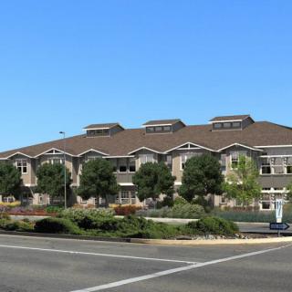 A modern building with a landscaped exterior and adjacent road under a clear blue sky.