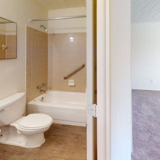 A bathroom featuring a bathtub, toilet, and mirror with an adjoining living area.