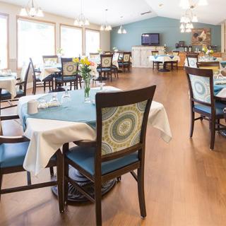 A well-lit dining area with elegantly set tables and chairs, featuring wooden flooring and modern decor.
