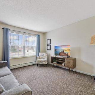 A cozy living room with a large window, sofa, armchair, and a television.