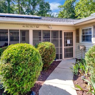 A welcoming entrance to a cozy house, featuring a neatly landscaped front yard with bushes and a paved pathway leading to a screened door.