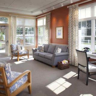 A cozy living room with a sofa, chairs, and large windows letting in natural sunlight.