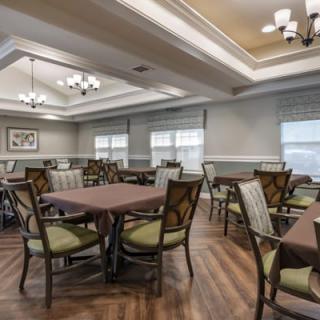A well-lit dining room with multiple tables and chairs, featuring elegant light fixtures and wooden flooring.