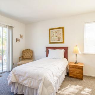 A bright bedroom with minimalist decor featuring a single bed, nightstand, and armchair.