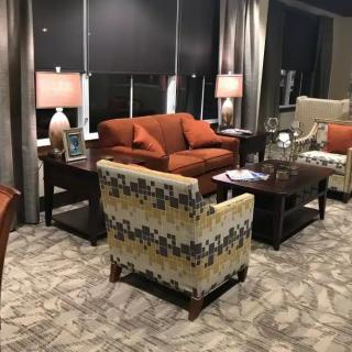 A cozy living room with a patterned armchair, an orange sofa, and warm lighting from table lamps.