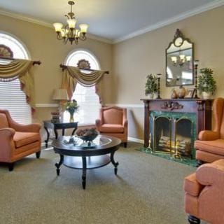 A cozy, traditionally decorated living room featuring a fireplace, elegant armchairs, and a chandelier.