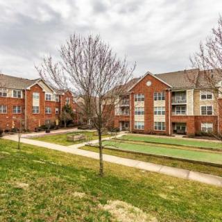 A residential apartment complex with a brick exterior, surrounded by trees and a neatly manicured lawn.