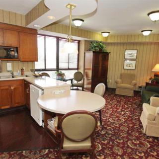 A cozy indoor space with a kitchen and dining area featuring wooden cabinets, a round table, chairs, and a patterned carpet.