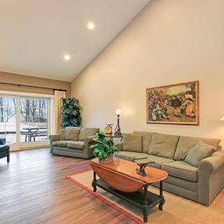 A spacious living room with high ceilings, featuring comfortable sofas, a wooden coffee table, artwork on the walls, and large windows overlooking a scenic view.