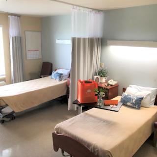 A view of a hospital patient room featuring two separate beds, curtains for privacy, and basic furnishings.