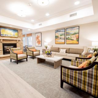 A cozy and elegantly decorated living room featuring a sofa, armchairs, and a fireplace with artwork on the walls.