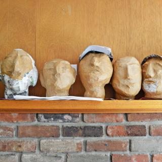A display of plaster head sculptures on a wooden shelf against a brick wall.