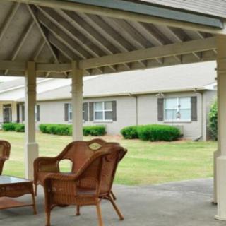 A covered patio with wicker chairs overlooking a lawn and building.