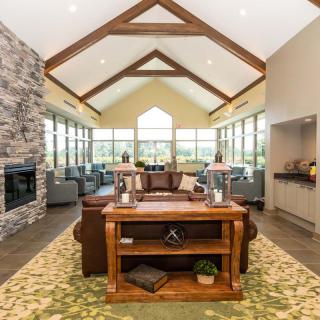 A spacious living room featuring a vaulted ceiling with wood beams, a stone fireplace, and modern furnishings, illuminated by natural light from large windows.