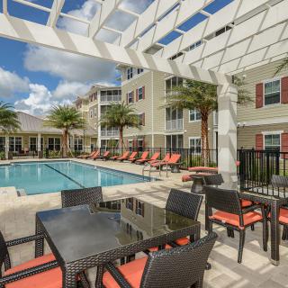 A sunny outdoor pool area with lounge chairs and patio furniture at an apartment complex.