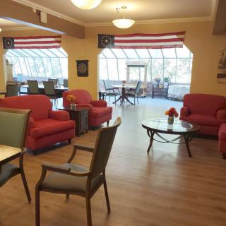 A cozy seating area with red sofas, chairs, and tables under a large window adorned with flags.