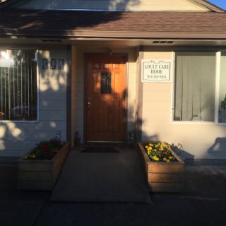 A house entrance with a wooden door and planters, illuminated by sunlight.