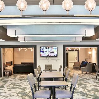 A modern lobby with a seating and dining area, featuring elegant chandeliers and a television on the wall.