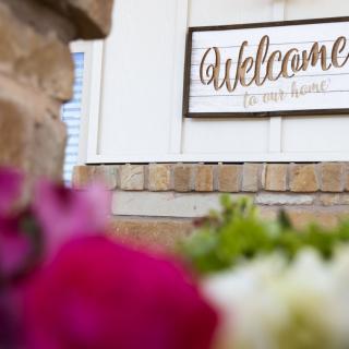 A welcoming sign on a brick wall surrounded by vibrant flowers.