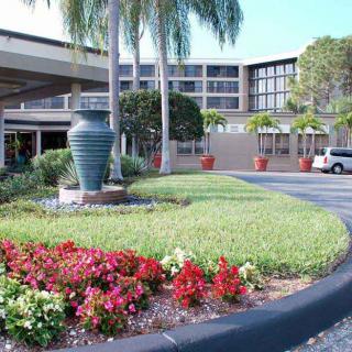 The exterior of a hotel featuring landscaped gardens and palm trees at the entrance.