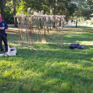 A person in a park stands next to a dog, while another object is visible on the ground nearby.