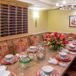 An elegantly set dining table with floral arrangements and upholstered chairs in a warmly lit room.