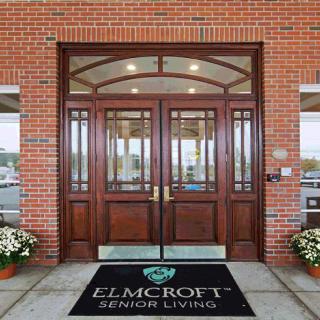 Entrance to Elmcroft Senior Living with double wooden doors and flower pots.