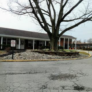 A view of a building surrounded by landscaping and a large tree, set against a cloudy sky.