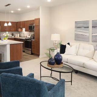 A modern open-layout living room with a connected kitchen, featuring a white sofa, blue chairs, and decorative elements.